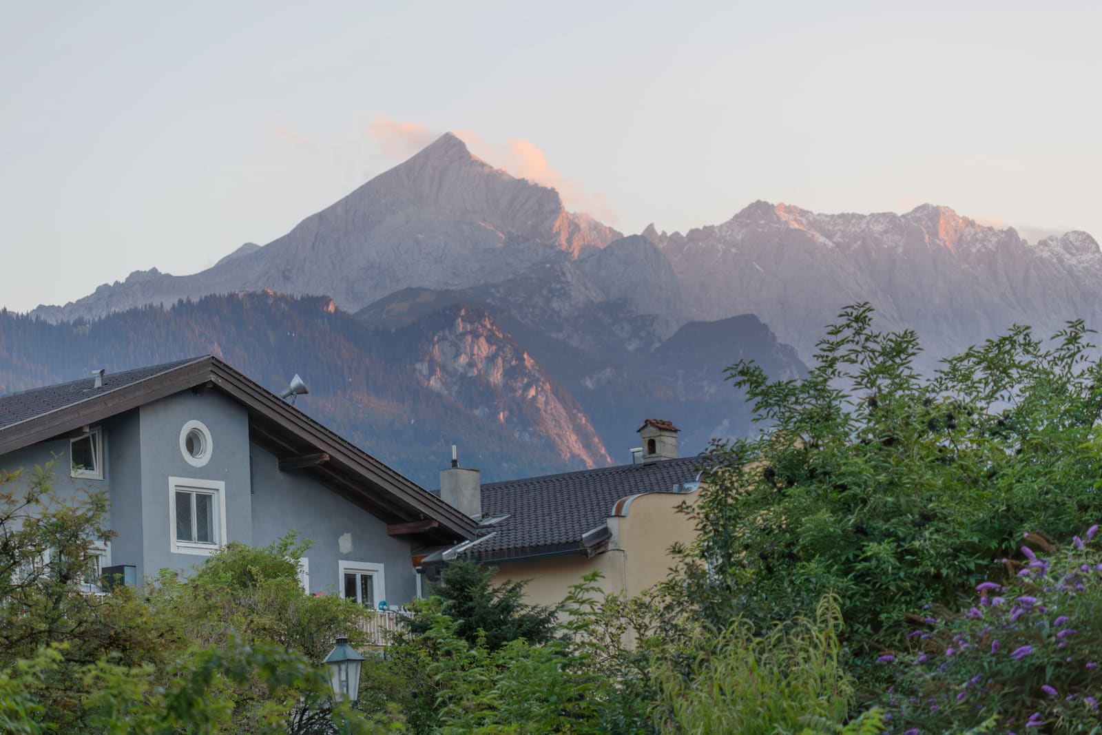 Wohnhäuser und Gärten in Garmisch-Partenkirchen vor einem im Abendlicht leuchtenden Alpenmassiv