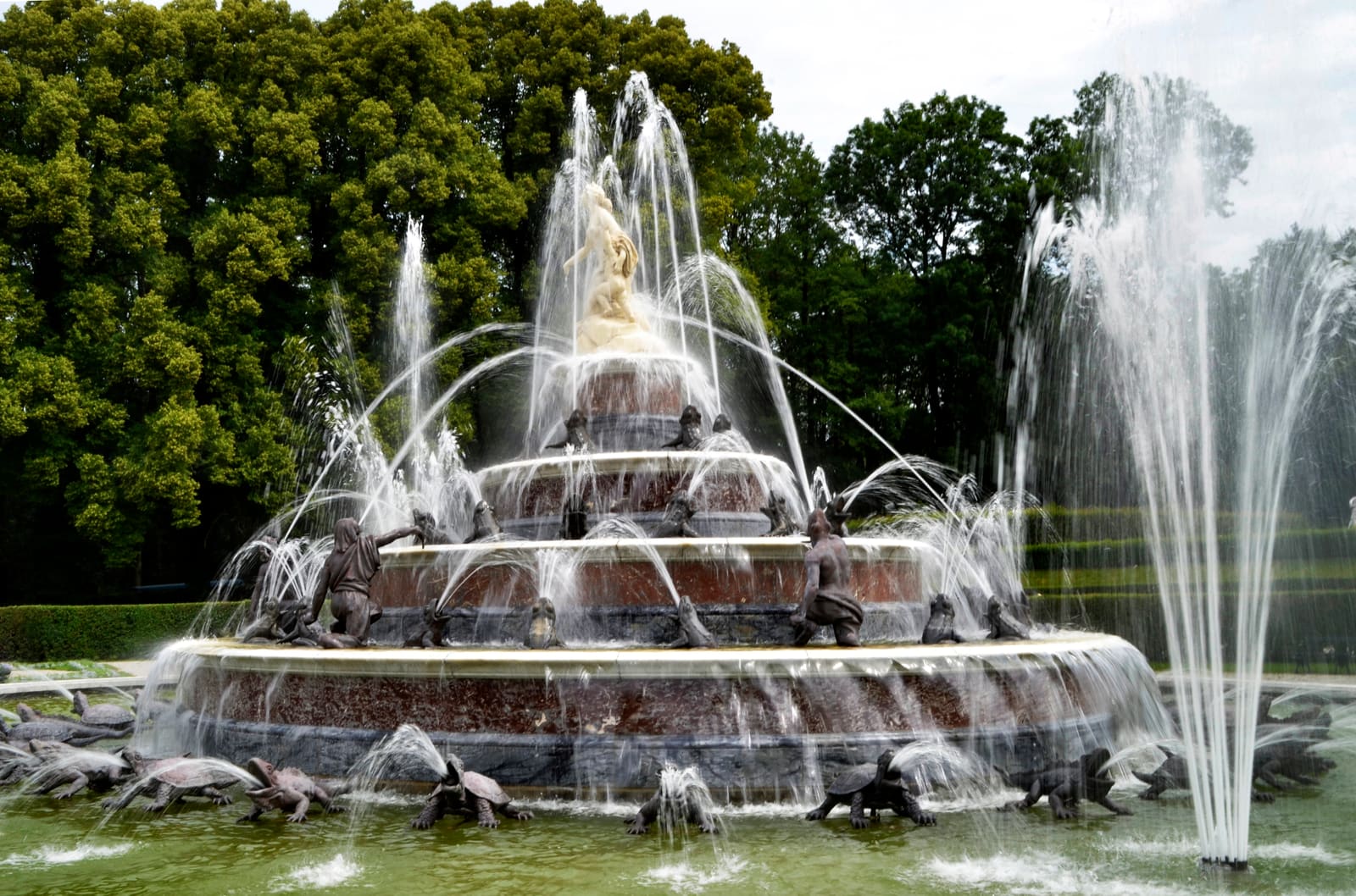 Der Latonabrunnen im Schlosspark Herrenchiemsee: die vergoldete Latona auf der obersten Stufe, darunter Bronzefiguren in Verwandlung und hohe Wasserfontänen