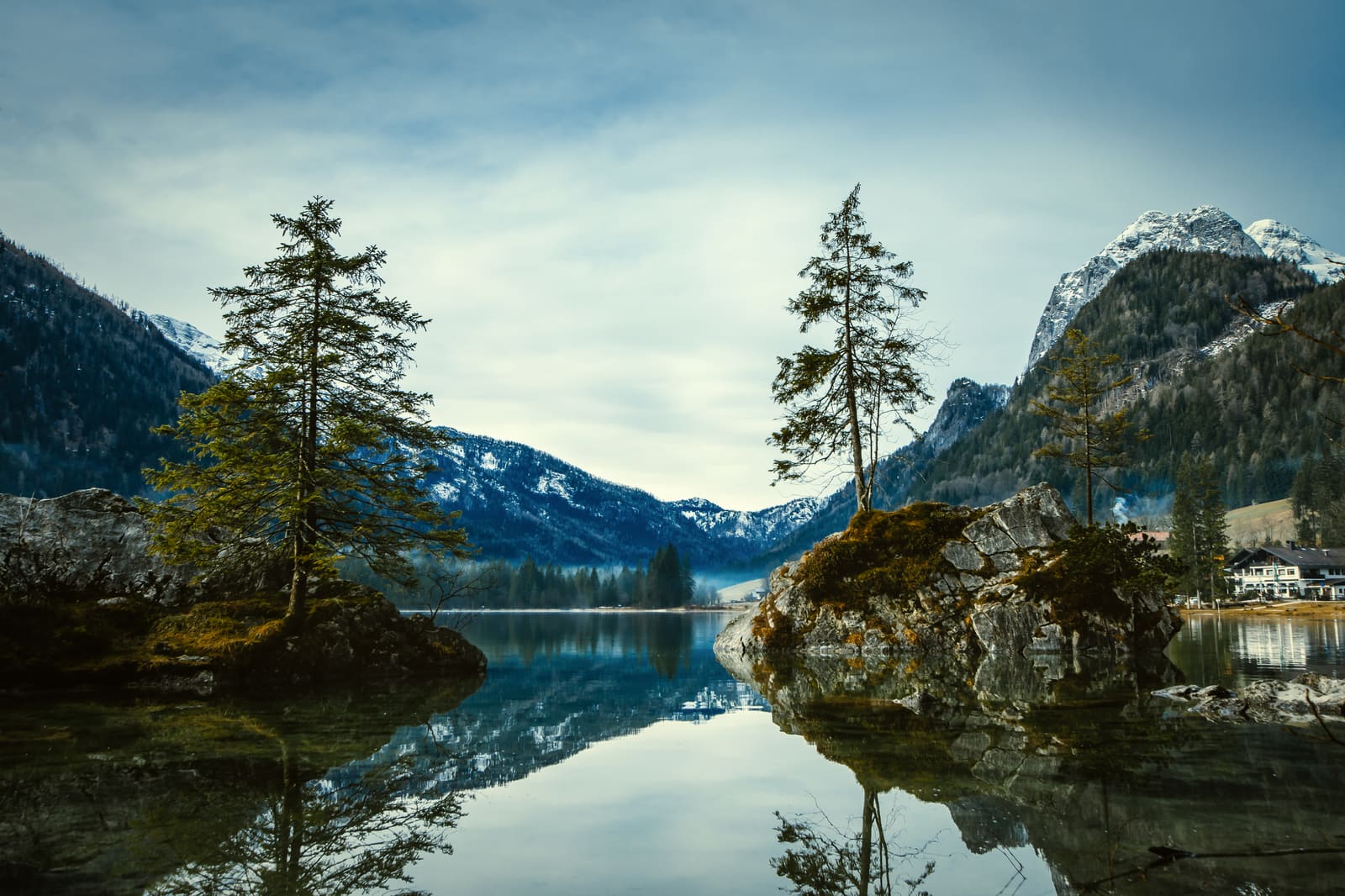 Der Hintersee bei Berchtesgaden mit bewaldeten Felsen, ruhiger Spiegelung und verschneiten Berggipfeln