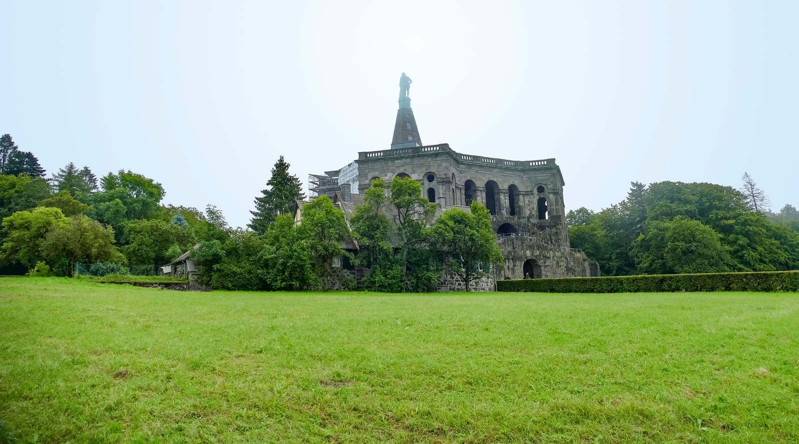Herkulesmonument im Kasseler Bergpark Wilhelmshöhe über einer weiten grünen Wiese und umgeben von dichtem Parkwald