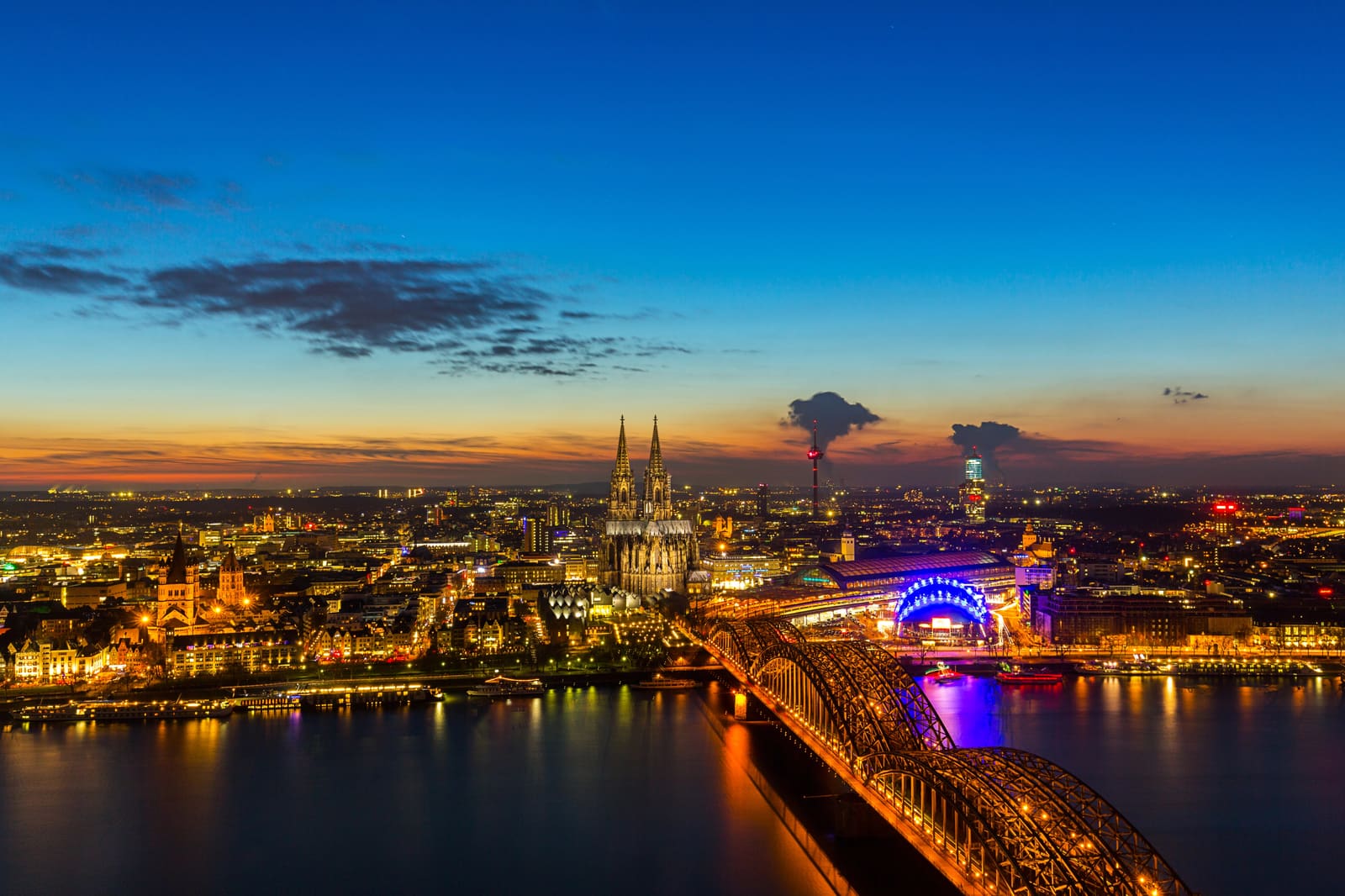 Abendlicher Blick über den Rhein auf den beleuchteten Kölner Dom, die Hohenzollernbrücke und das Stadtzentrum