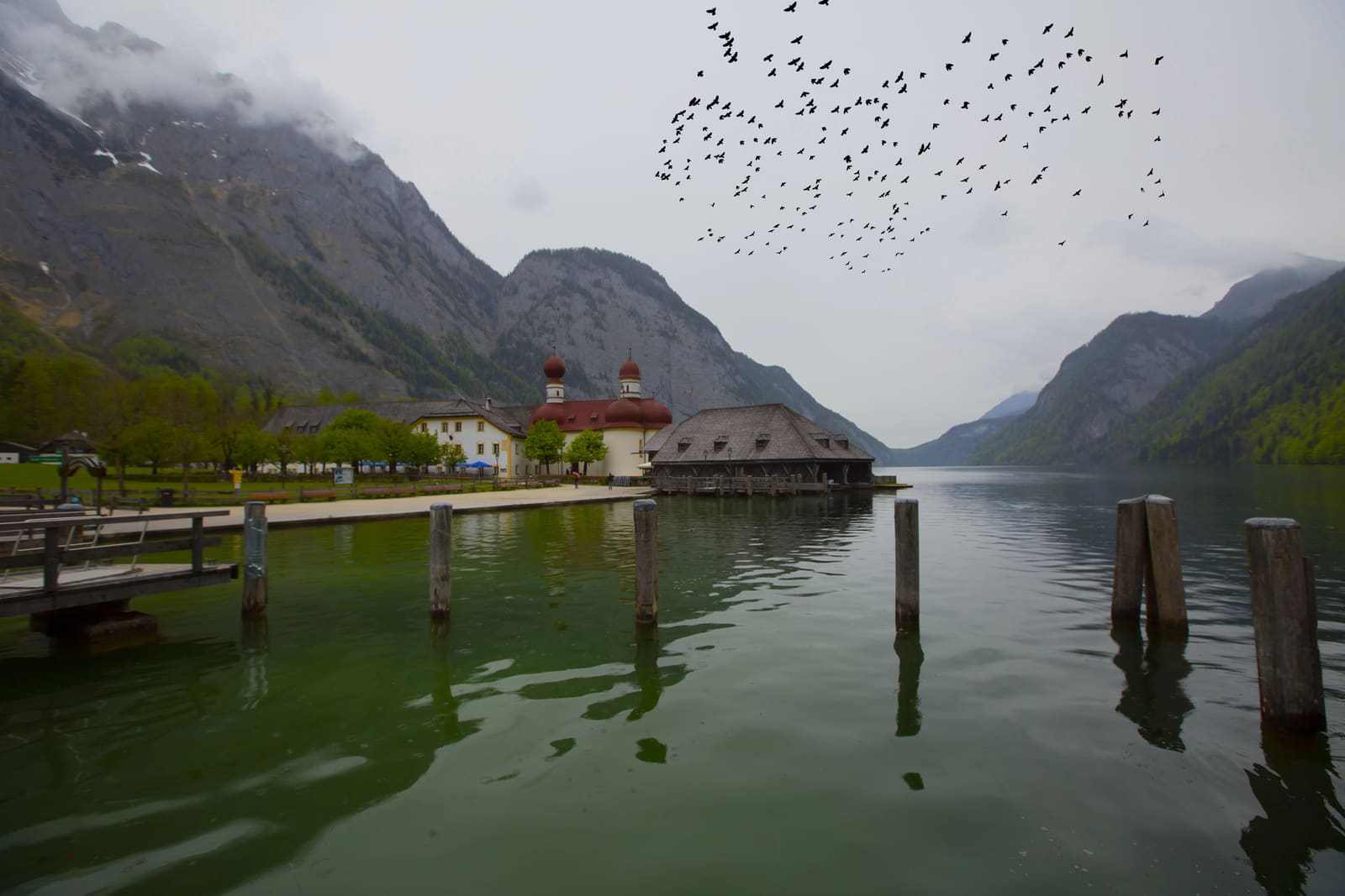 Wallfahrtskirche St. Bartholomä und historisches Bootshaus am Königssee unter wolkenverhangenen Berghängen