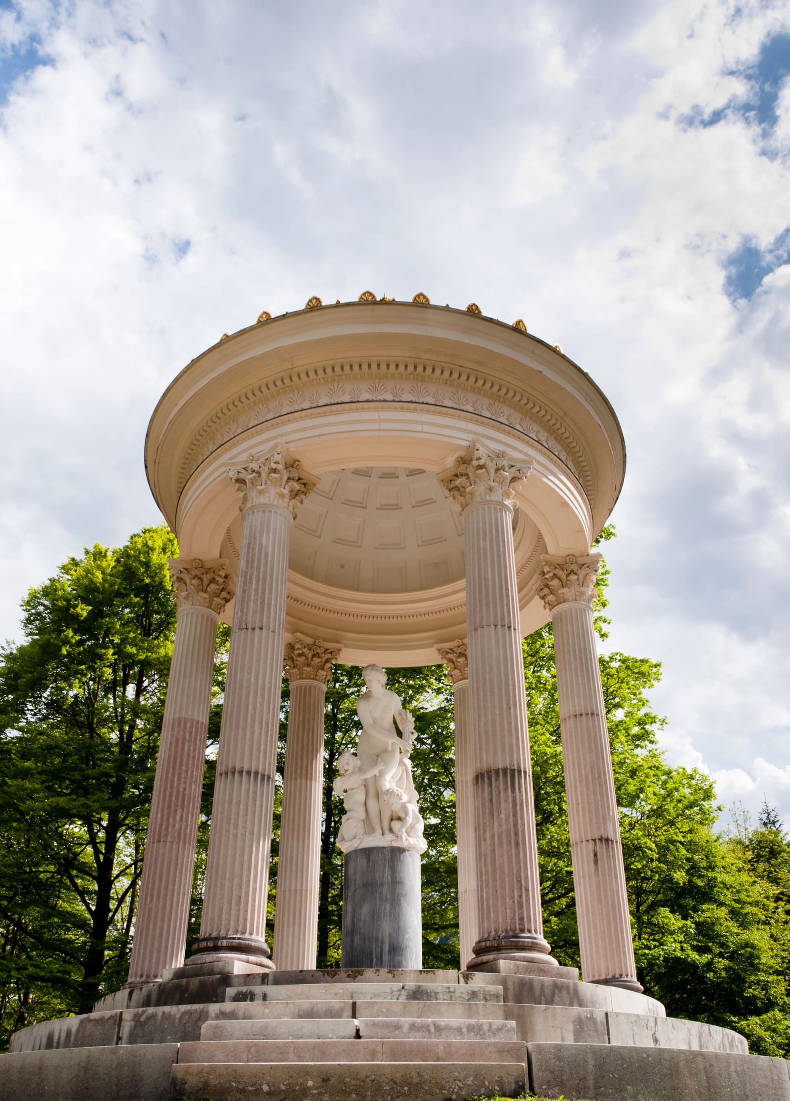 Runder Venustempel im Schlosspark Linderhof mit korinthischen Säulen und Venusstatue vor grünen Bäumen