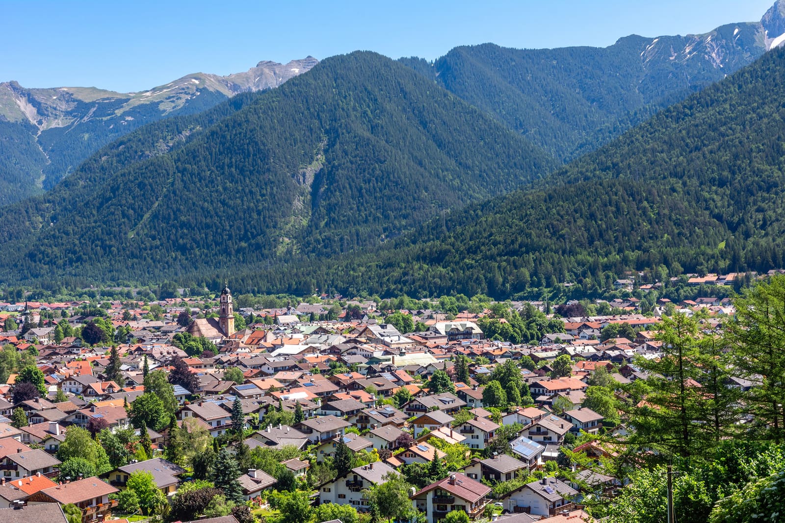 Blick über die Dächer von Mittenwald mit dem Zwiebelturm von St. Peter und Paul, dahinter bewaldete Berghänge