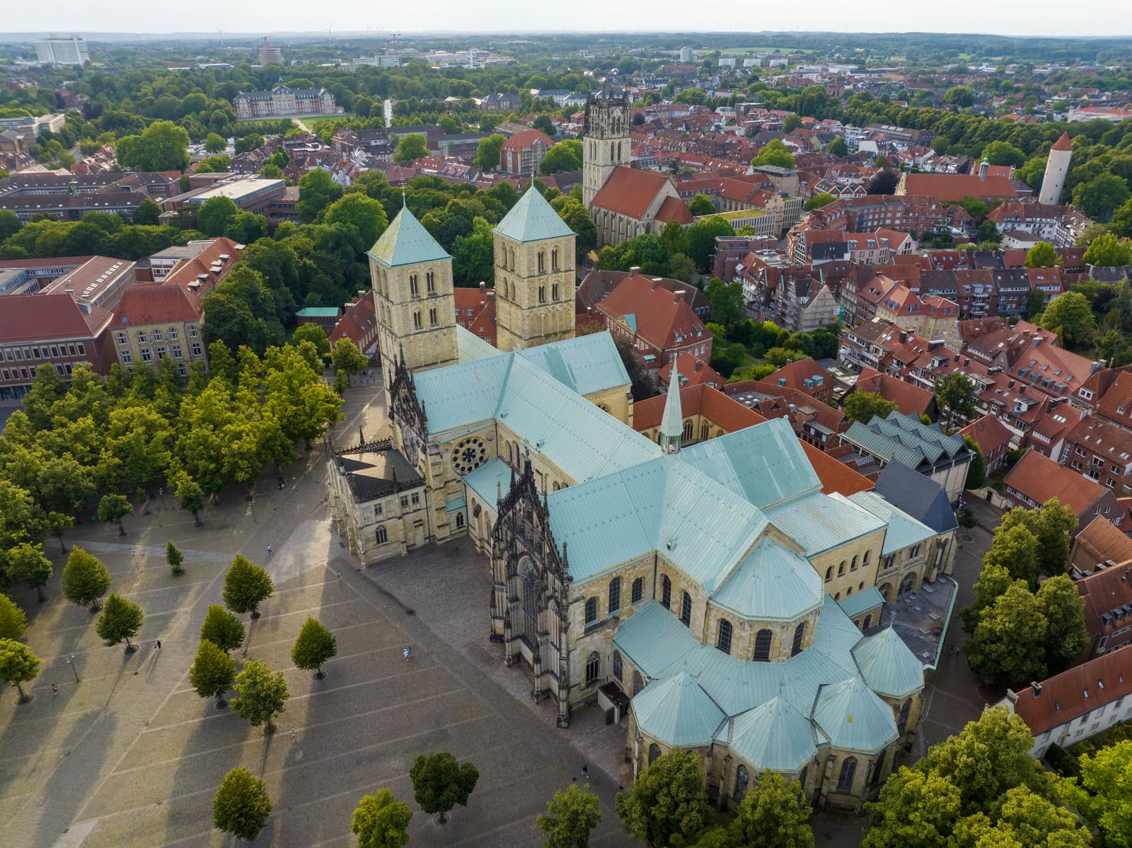 Luftbild des St.-Paulus-Doms mit seinen Doppeltürmen über dem grünen Domplatz und der roten Dachlandschaft von Münster