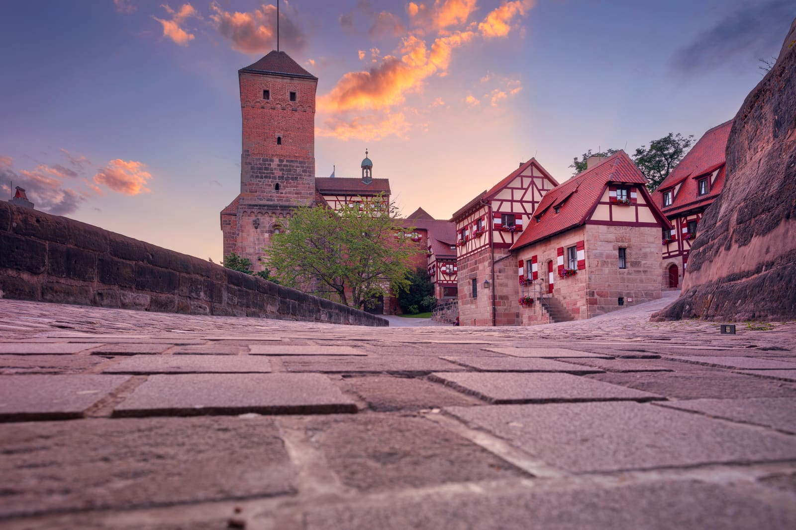 Kopfsteingepflasterter Zugang in der Nürnberger Kaiserburg mit Sinwellturm und Fachwerkgebäuden unter leuchtenden Abendwolken
