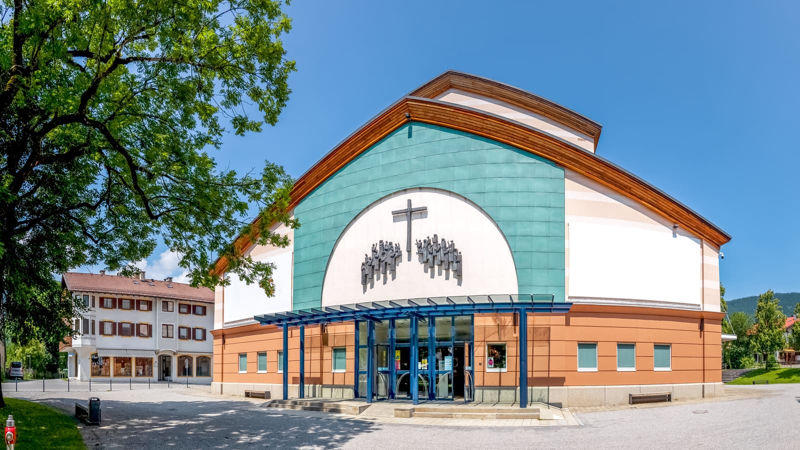 Frontansicht des Passionstheaters Oberammergau mit Kreuzigungsrelief, türkisfarbener Fassade und gläsernem Eingang