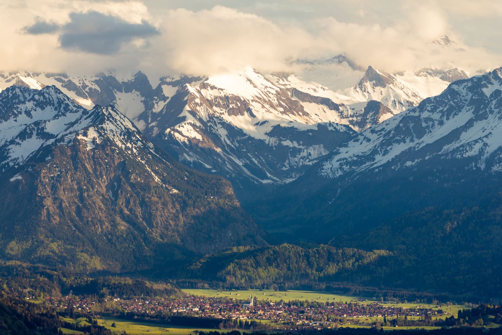 Oberstdorf im Illertal unter verschneiten Allgäuer Hochalpen und dramatischen Wolken im warmen Abendlicht