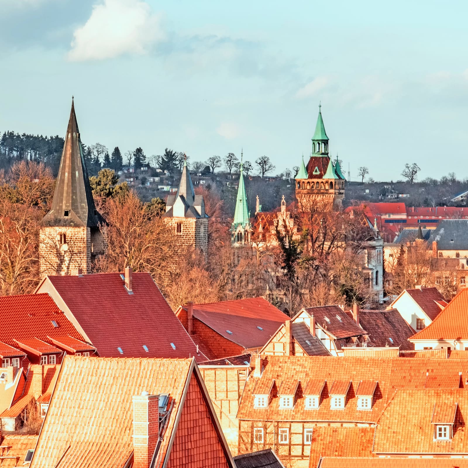 Blick über rote Ziegeldächer und Fachwerkhäuser der Quedlinburger Altstadt zu mehreren historischen Kirchtürmen