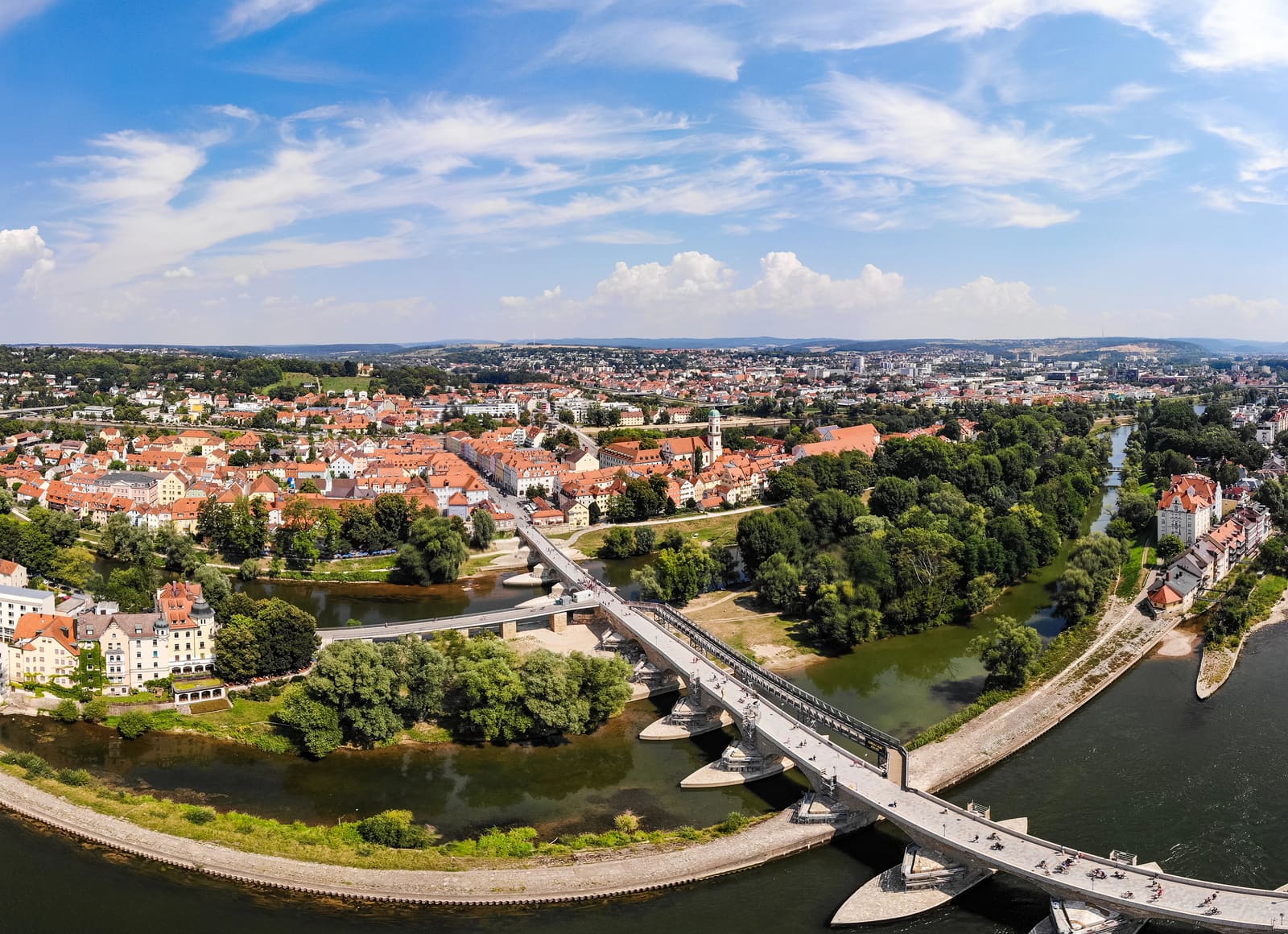 Luftpanorama von Regensburg mit einer Brücke über die Donau, begrünten Inseln und roten Dächern der Stadt