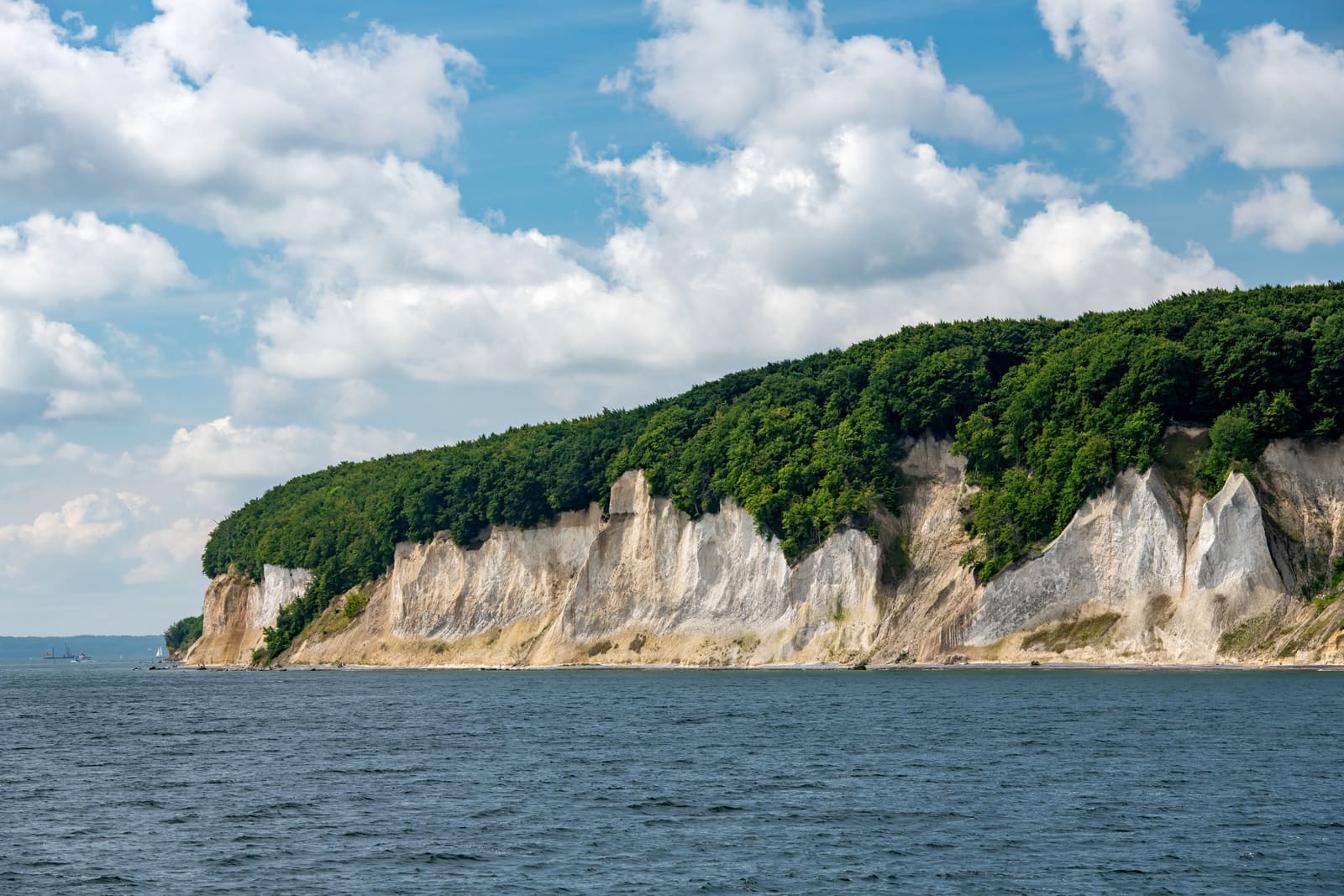Weiße Kreidefelsen an der bewaldeten Küste von Rügen über der blauen Ostsee unter sommerlichen Wolken