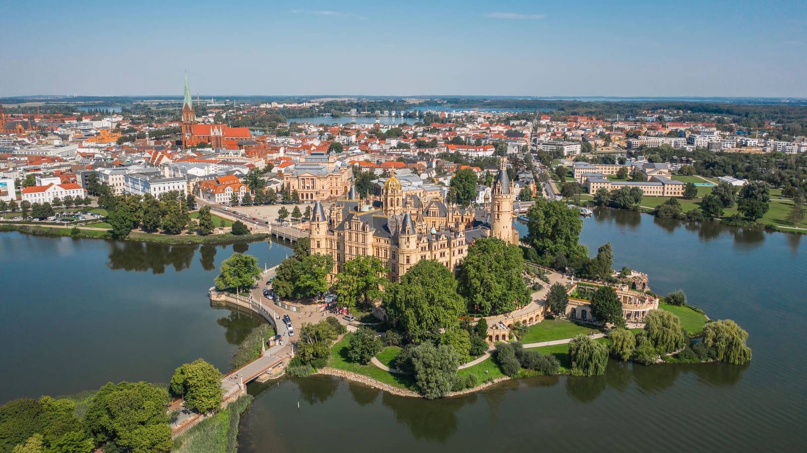 Luftbild des Schweriner Schlosses auf seiner Insel im Burgsee mit Schlossgarten, Altstadt und weiteren Seen im Hintergrund