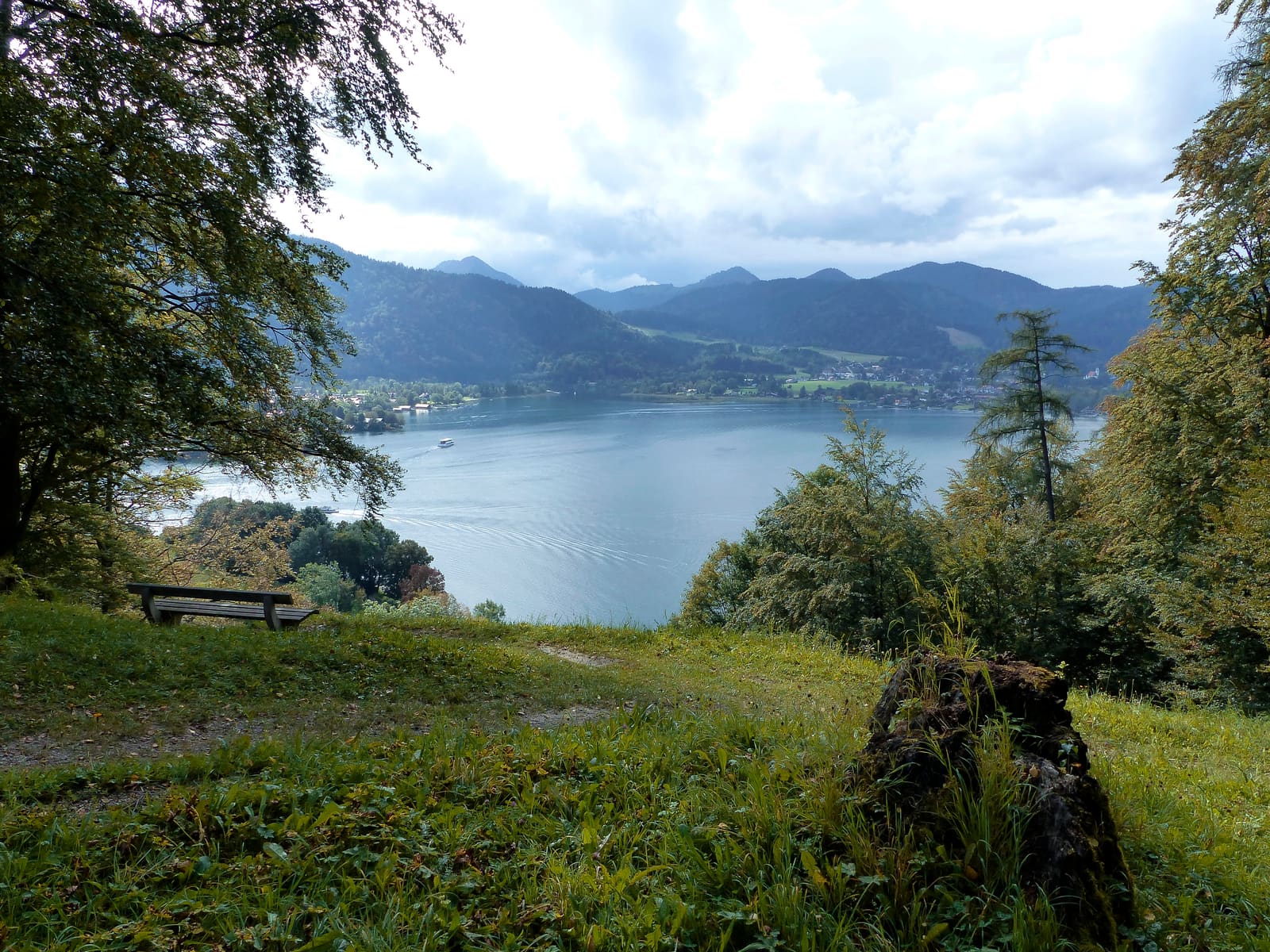 Waldlichtung mit Sitzbank und weitem Blick über den Tegernsee zu den bewaldeten Bergen und Uferorten