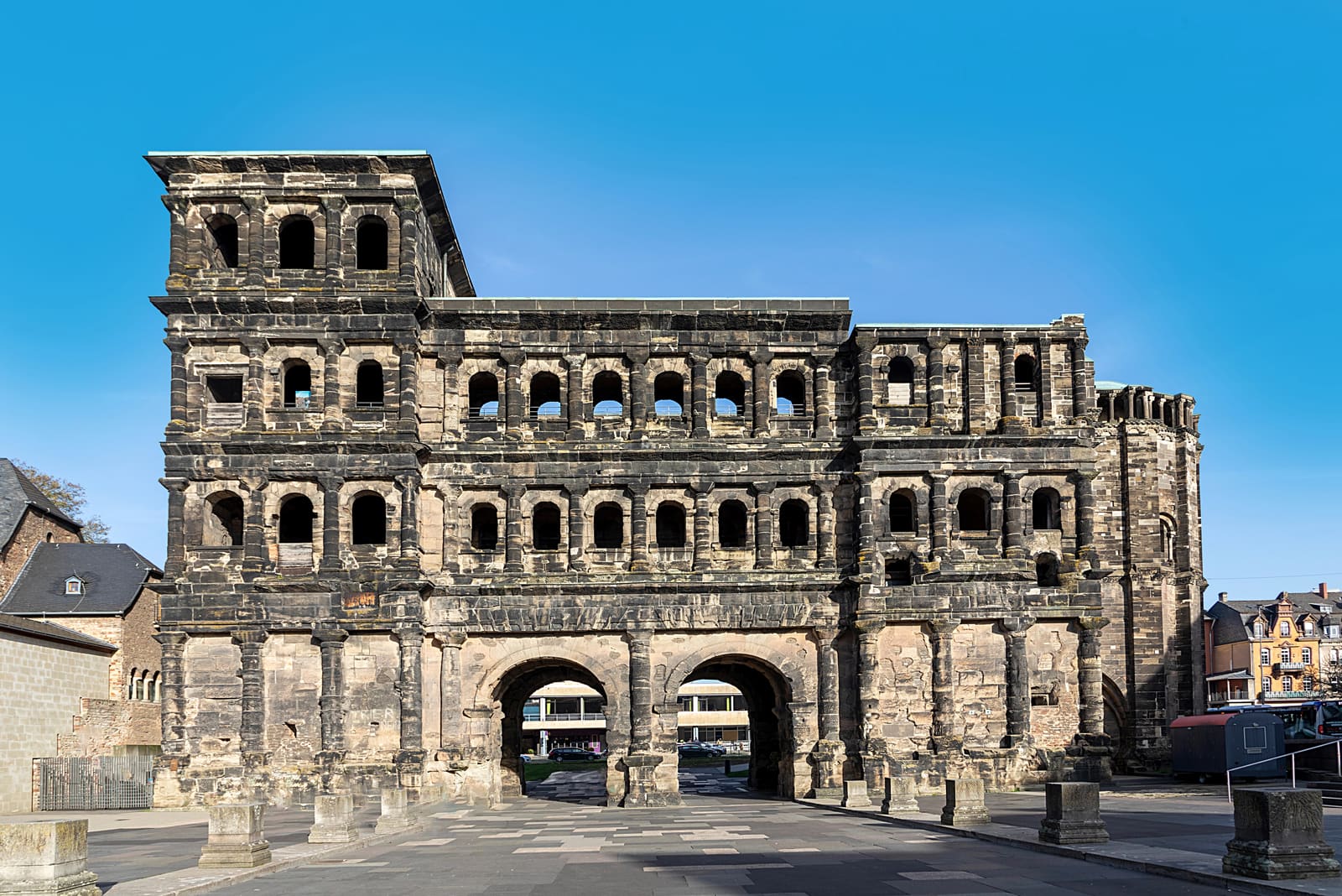 Monumentale dunkle Sandsteinfassade der Porta Nigra in Trier mit Rundbogenfenstern und zwei Durchfahrten unter blauem Himmel