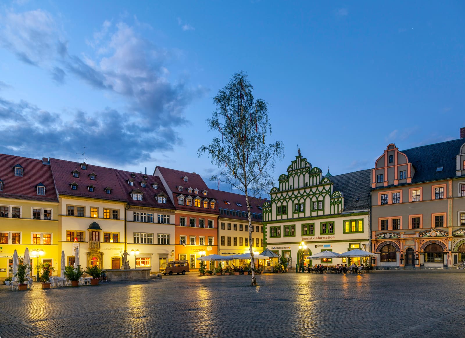 Beleuchtete historische Bürgerhäuser am Weimarer Marktplatz mit Tourist-Information, Neptunbrunnen und nassem Kopfsteinpflaster am Abend