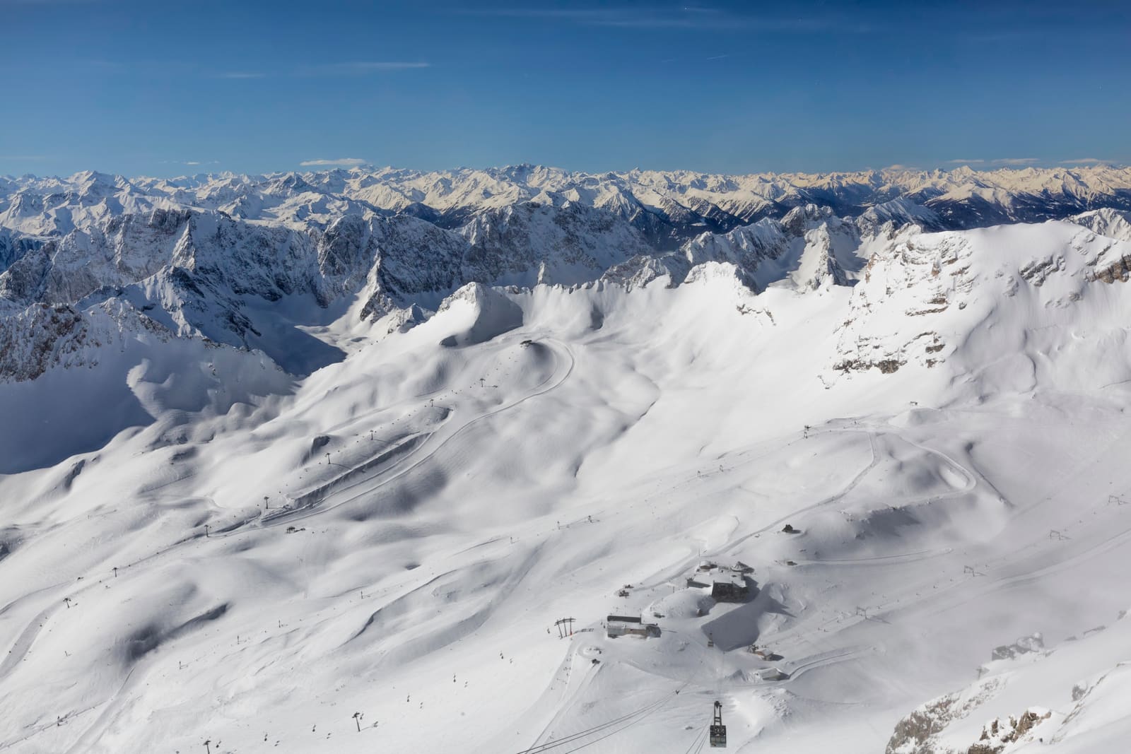 Verschneites Zugspitzplatt mit Gletscherflächen, Skipisten, Liftanlagen und weitem Alpenpanorama unter blauem Himmel